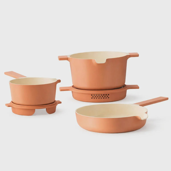Set of peach-colored cookware set including pots and a pan on a white background