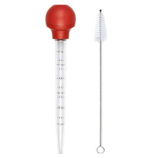 Red turkey baster with clear tube and cleaning brush on a white background