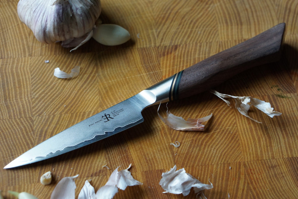 Paring knife with wooden handle on a wooden surface with garlic cloves